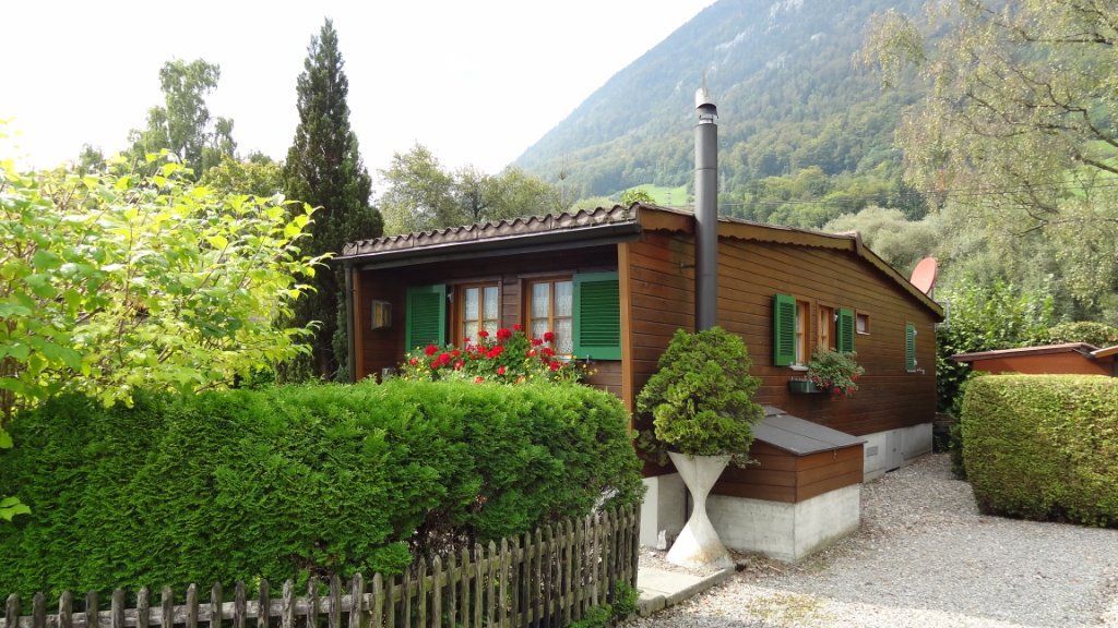 Holzhaus mit grünen Fensterläden und Bergwald im Hintergrund